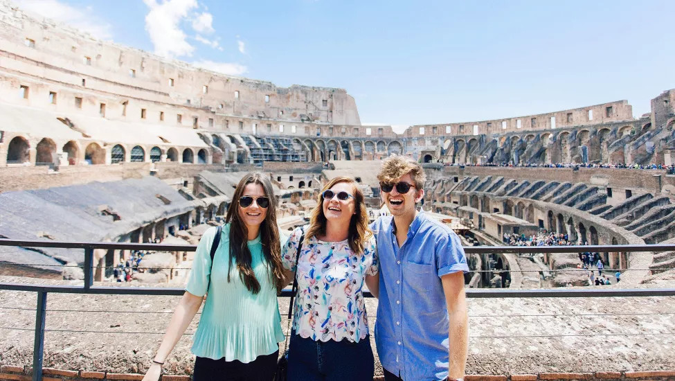 Three people stand together smiling while standing inside the Colosseum in Rome.