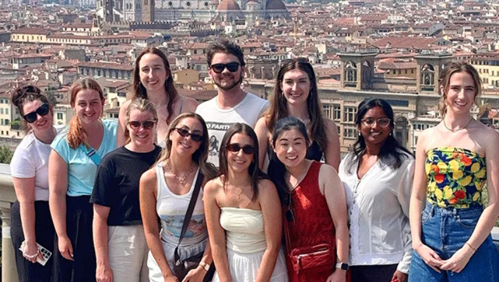Group of people stand together smiling on a view point in Florence with the Cattedrale di Santa Maria del Fiore in the distance.