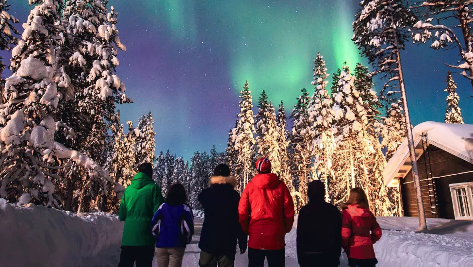 People standing in the snow at night with the northern lights in the sky.