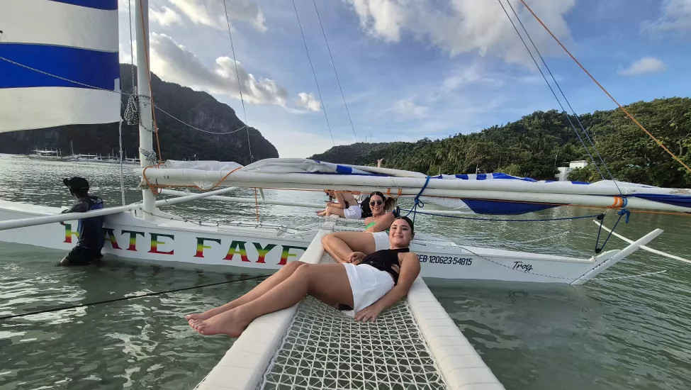 Two girls lay on the netting of a slim catamaran in the Philippines.