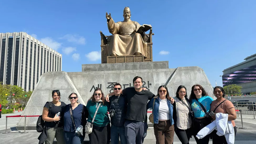 Small group of people smile together in front of Statue of King Sejong the Great in Gwanghwamun Square.