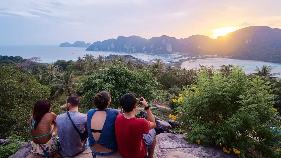 People sitting together on a large rock watching the sunrise in the Phi Phi Islands.
