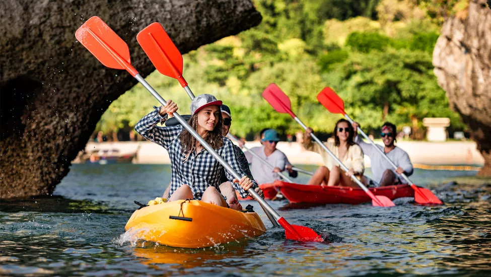 Group of people paddling two seater kayaks near a beach in Thailand.