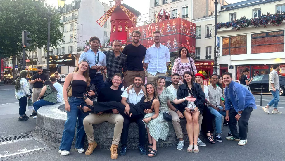 Group of people pose together in front of the Moulin Rouge cabaret in Paris.