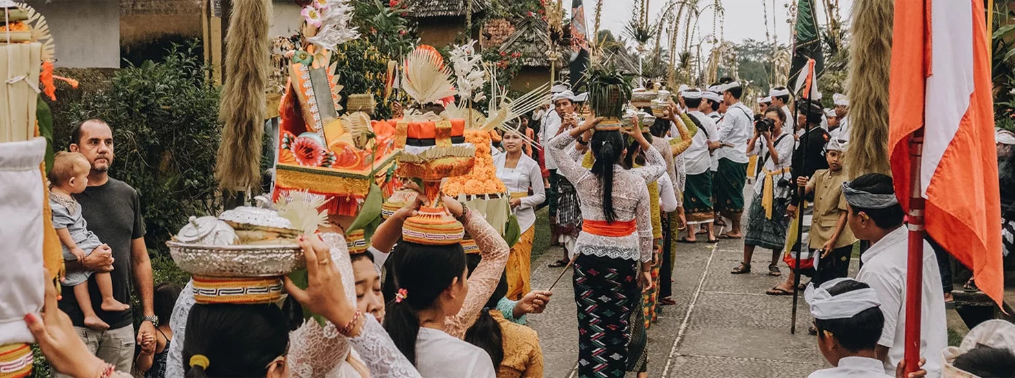 Bali people holding fruit on top of their heads parading down a road celebrating the day of silence.