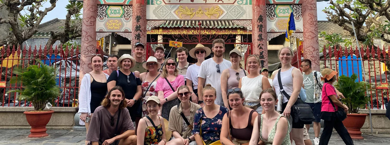 A Topdeck tour group poses for a group photo in front of an old assembly hall in Cambodia.