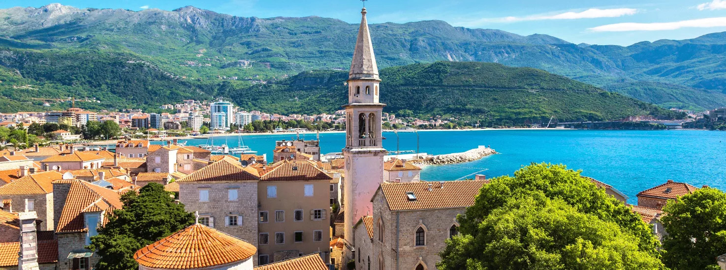 View of the coastal town of Budva with its orange rooves and nearby mountain range.