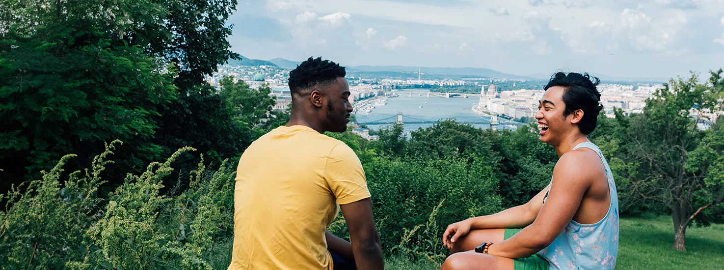 Two male Topdeck travelers laughing and joking with each other with a landscape view of Budapest in the background.