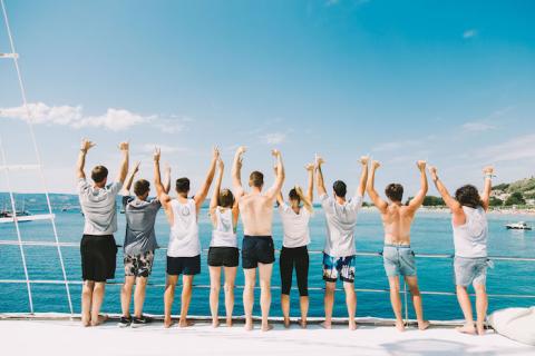 A group of people on a boat with their arms in the air looking out to sea