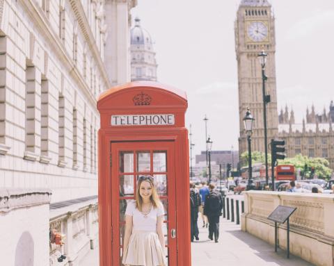 A woman standing in front of a red telephone box, with Big Ben in the background