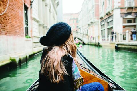 The back of a woman sitting in a canal boat in Venice