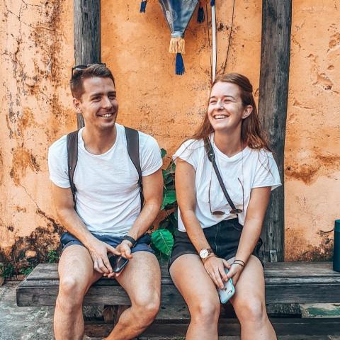 Man and a woman sitting on a bench smiling, they both wear white t-shirts