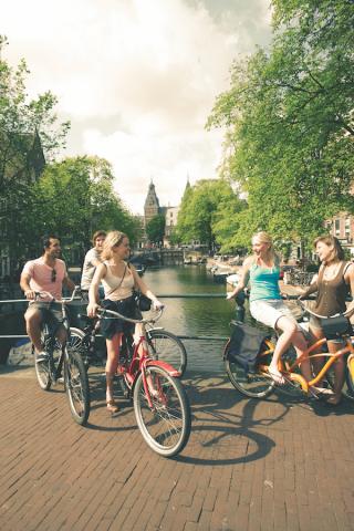 five friends sitting on their bikes stationary in Amsterdam. The canal is behind them
