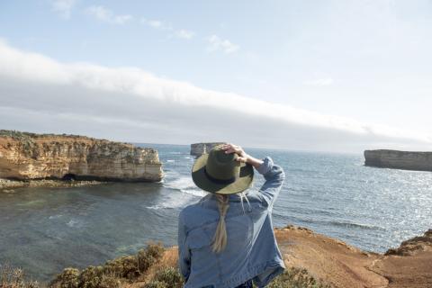 Woman wearing a hat facing away from the camera staring into the sea in Australia
