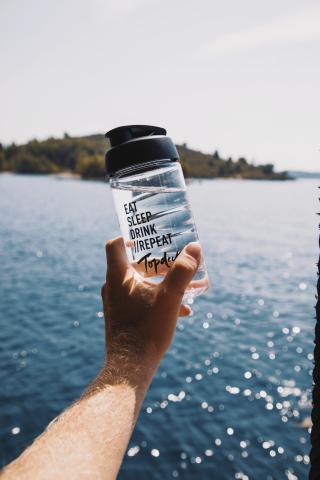 A person holding a water bottle that reads 'Eat, Sleep, Drink, Repeat' and then the Topdeck logo