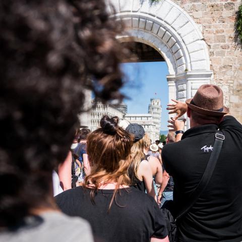 This pictures looks over the shoulder if someone with dark brown curly hair. We can see an archway and people walking through it