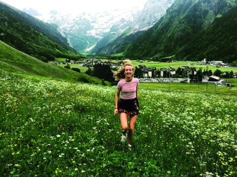 A woman running through a field of flowers, with Swiss mountains in the background