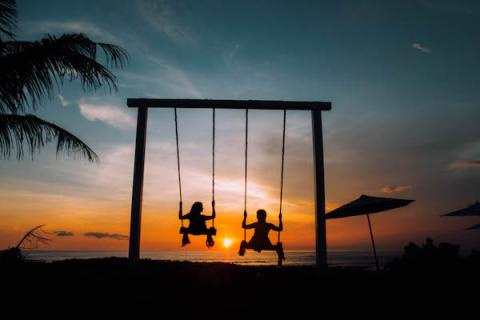 two silhouette figures on swings in the sunset