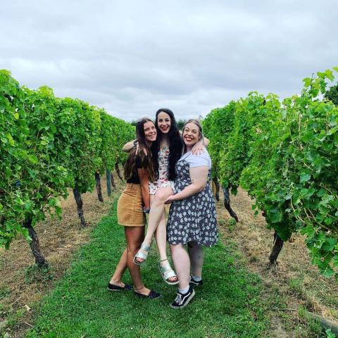 Two women holding up another women between them in a vineyard