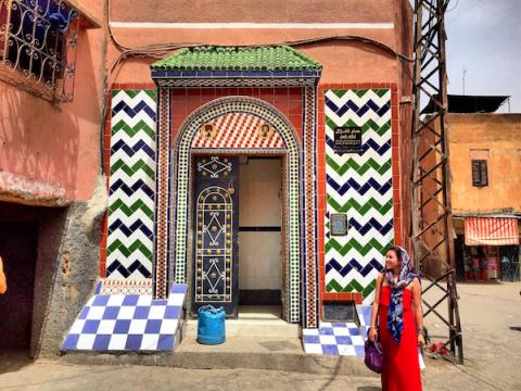 A tiled and decorated house in Morocco, with a woman standing in front of it wearing a head wrap