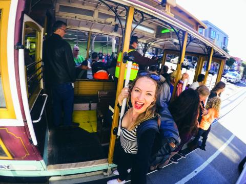 A woman hanging onto a moving tram in San Francisco