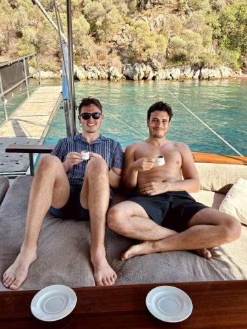 Two men sitting on a boat smiling, drinking Turkish tea