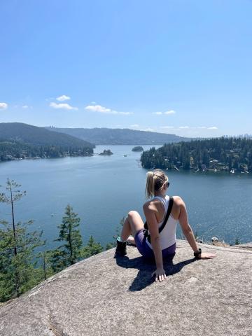Woman sitting on a large rock, looking out to a lake