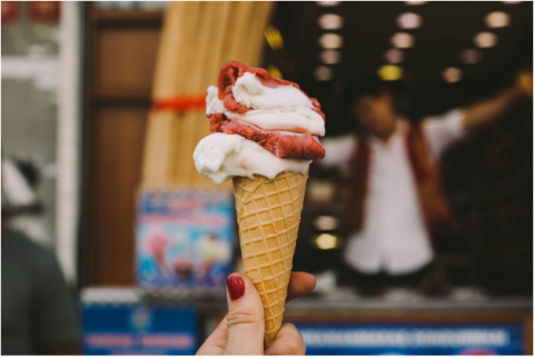white and red ice cream in a cone being held in front of an ice cream shop