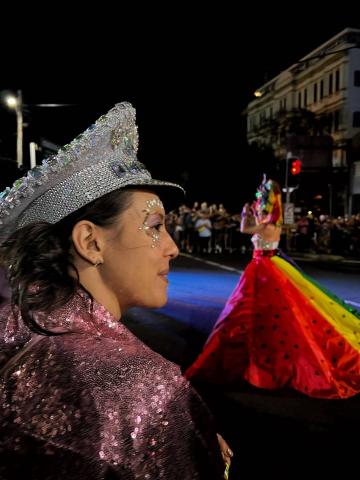 A person wearing a rainbow dress in the background and a person in glitter and jewels in the foreground