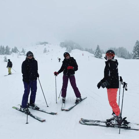 Three people standing in the snow in skis