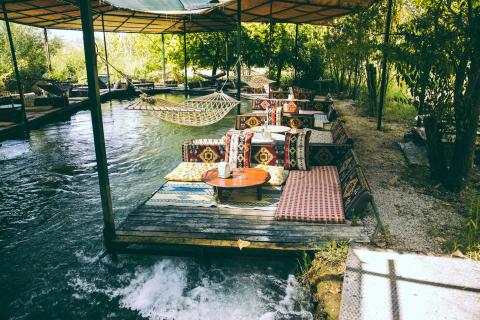 wooden platform with a small table and blankets above water to drink tea