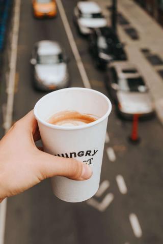 A person holding a cup of coffee in a takeaway cup