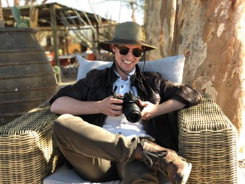 A man smiling sitting down on a chair looking at the pictures he's taken on his camera