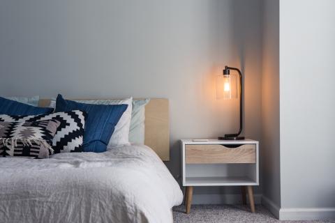 A made bed with many pillows on it. A bedside table is next to it, with a lamp on it