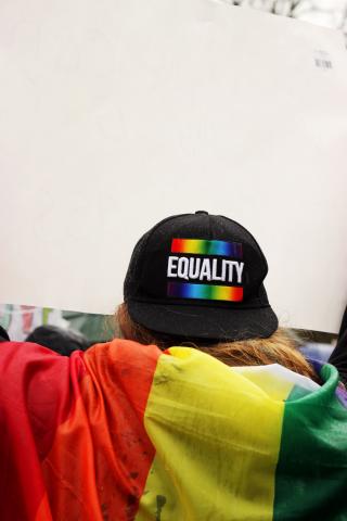 A person facing away from the camera. They are wearing a black cap that reads 'Equality' with a rainbow flag above and below the words