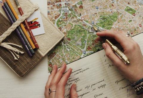 A person planning a holiday, writing in a notebook and pointing a pen at a map