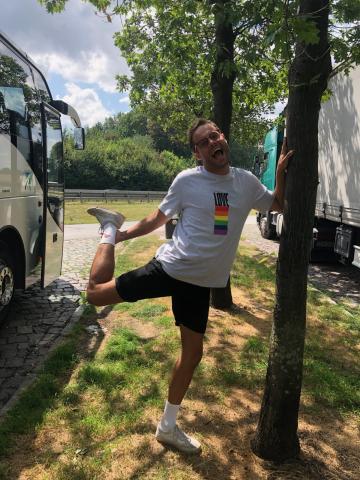 A man standing by a tree grinning wearing a Pride t-shirt