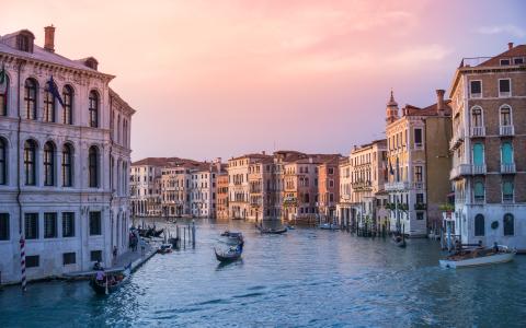 The Venice canal at sunset with boats on it and houses surrounding it