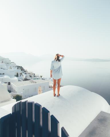 Woman standing on a white roof in Greece looking out to see