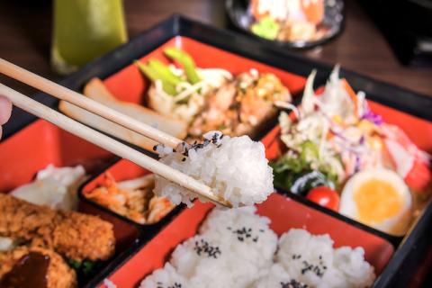 Chopsticks holding rice over a bento box