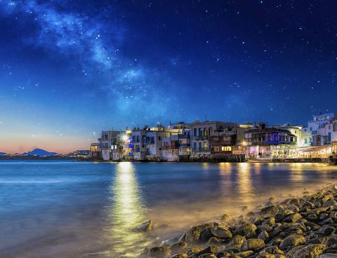 Houses by the sea at night. The sky is dark blue and starry