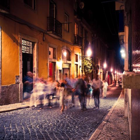 A group of people walking down a street in Portugal. They are blurry due to their movement