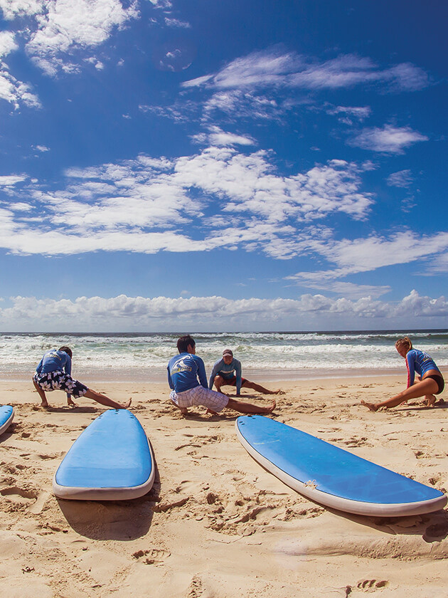 Topdeck travelers relaxing on a beach, with 2 surfboards in the foreground.