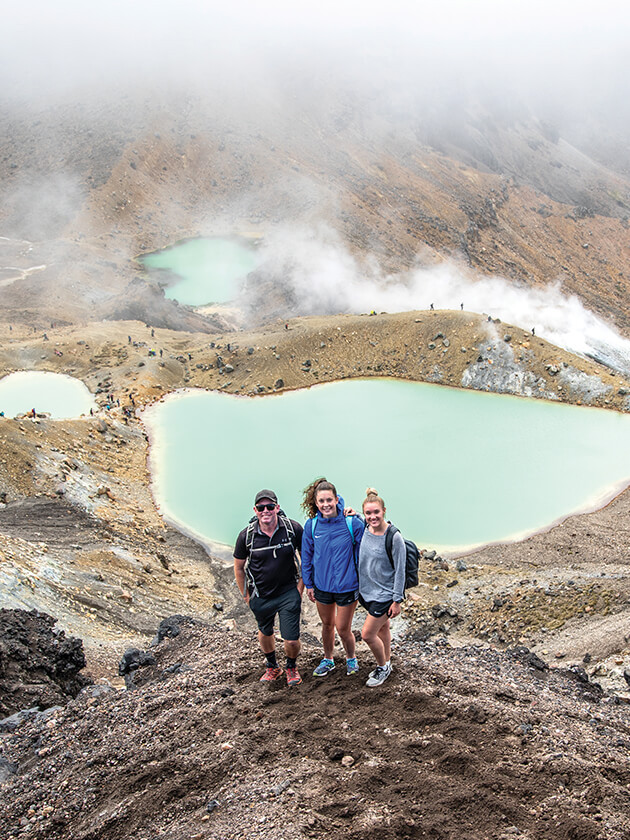 Three Topdeck travelers posing in front of volcanic area of the Tongariro National Park.