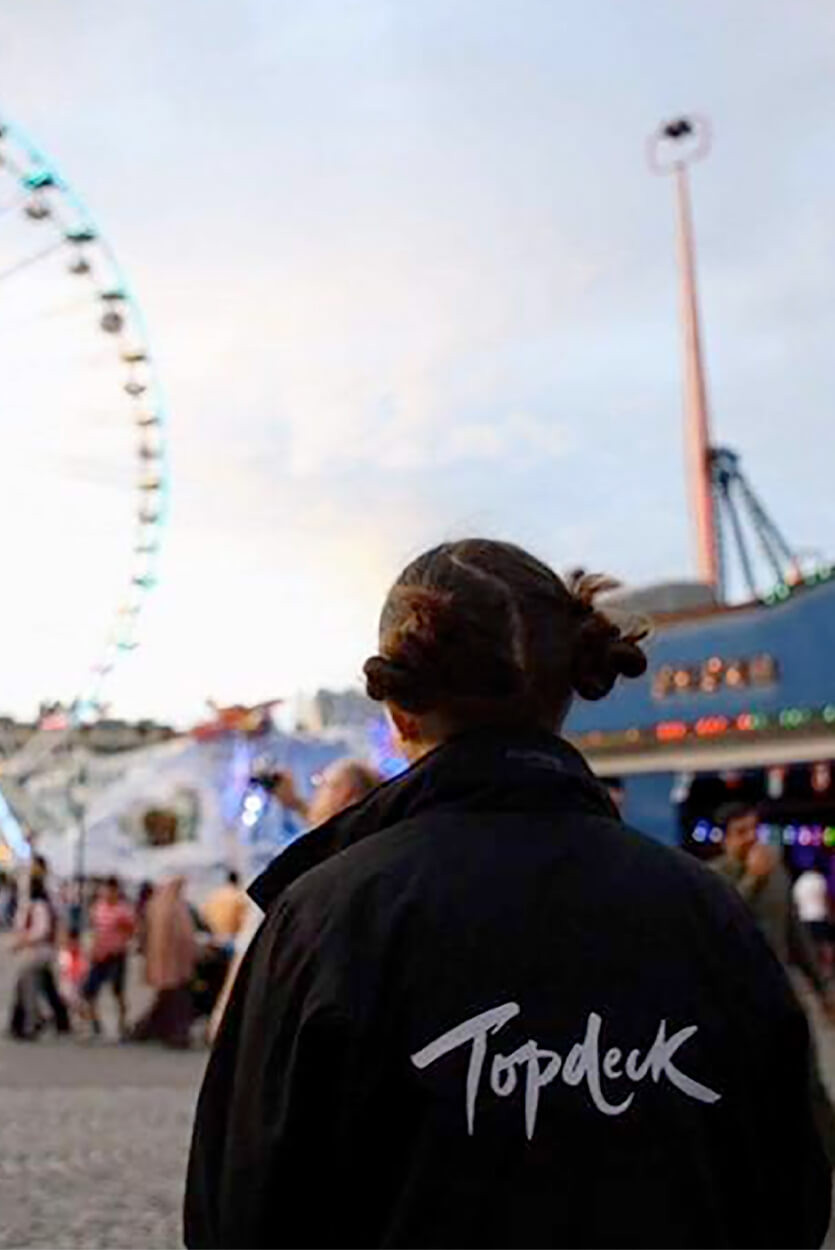 A Topdeck tour leader looking out over a fairground with many attractions.