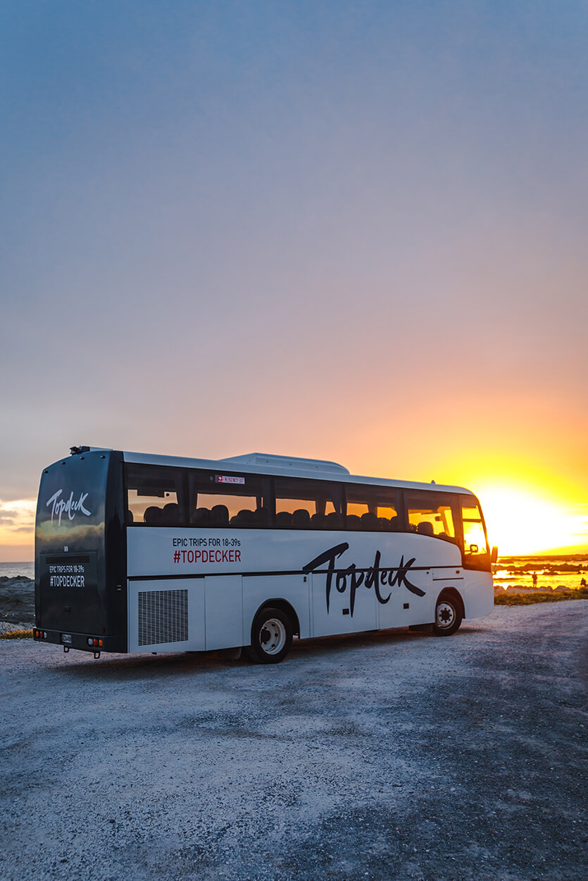 Topdeck tour bus driving off against the sunset.