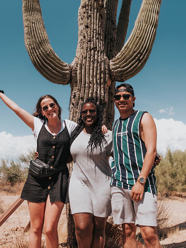 Three Topdeck Travelers posing in front of a cactus in Monument Valley.