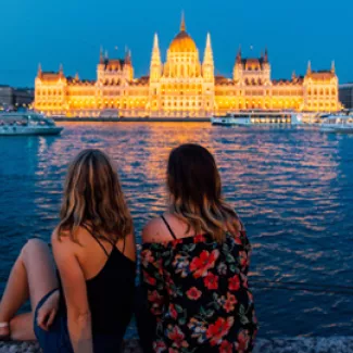 Two women look at the Hungarian Parliament building in Budapest at night