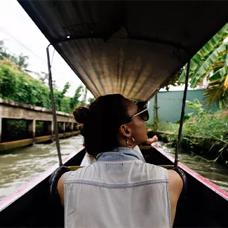 Person wearing sunglasses looks to their right while sitting in a narror wooden river boat.
