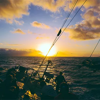 Sun setting on the horizon with the view of a sail boat in the foreground.